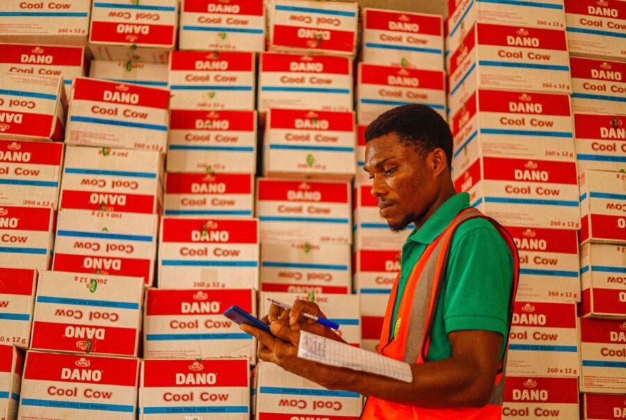 Jonge man met bruin haar met een tablet vast met allemaal dozen in zijn omgeving. hij is bezig met een voorraadtelling om de marge van de winkel direct te verhogen